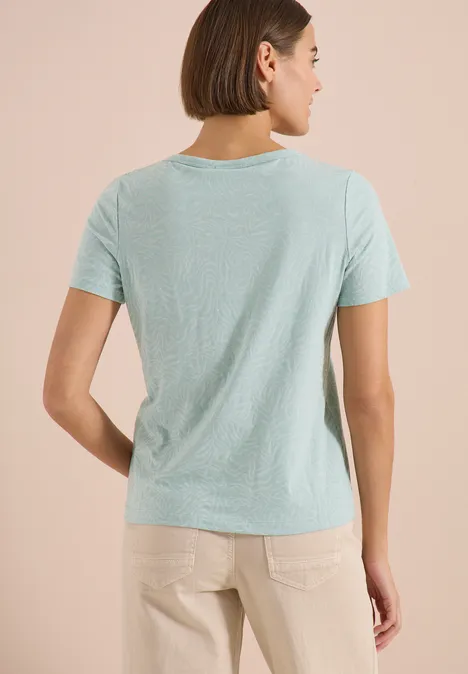 Kurzarm Shirt im Ausbrenner-Look crystal mint Rückansicht einer Frau in hellblauem T-Shirt und beigen Hosen vor beigem Hintergrund.