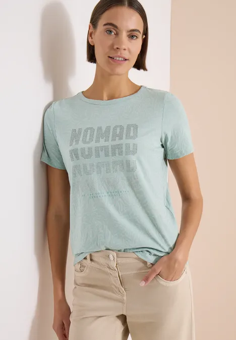 Kurzarm Shirt im Ausbrenner-Look crystal mint Eine Frau trägt ein mintgrünes T-Shirt mit 'Nomad Journal'-Print und beigen Hosen.