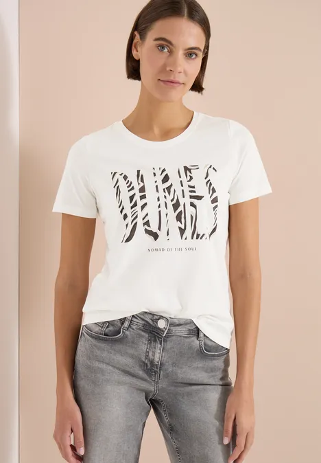 T-shirt à col rond et imprimé sur le devant vanilla white Frau trägt weißes T-Shirt mit Zebra-Print-Schriftzug und grauen Jeans.