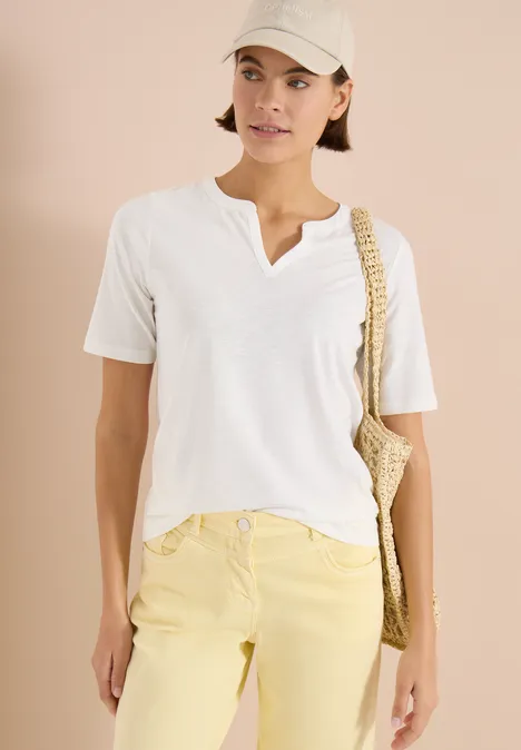 Person trägt weißes T-Shirt, gelbe Hose, weiße Schirmmütze und geflochtene Umhängetasche.