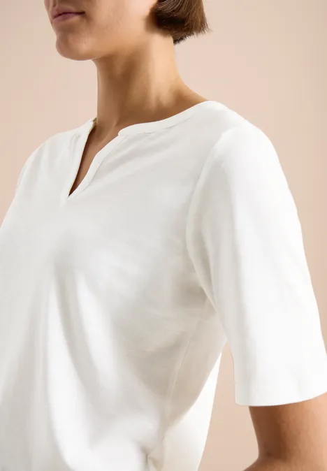 Oberkörper einer Person in schlichtem weißen T-Shirt mit V-Ausschnitt und halblangen Ärmeln.