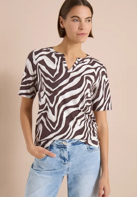 Vrouw draagt zwart-wit zebraprint top met korte mouwen en V-hals, gecombineerd met een lichtblauwe jeans.
