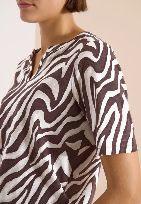 Een vrouw draagt een T-shirt met korte mouwen en bruin-witte zebraprint.