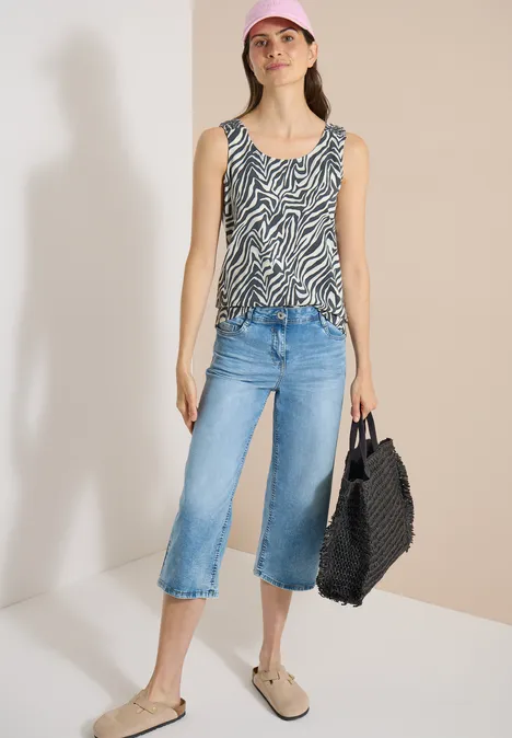 Haut à col rond et détails smockés palm breeze green Femme en débardeur zébré, jean large 3/4, mocassins et sac tressé noir sur fond clair.