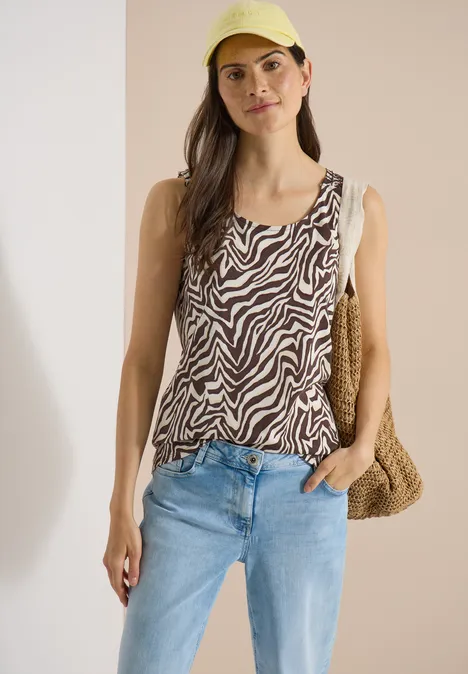 Haut à col rond et détails smockés brown cacao Femme portant un top zébré, jean bleu clair et sac en paille devant un fond neutre.