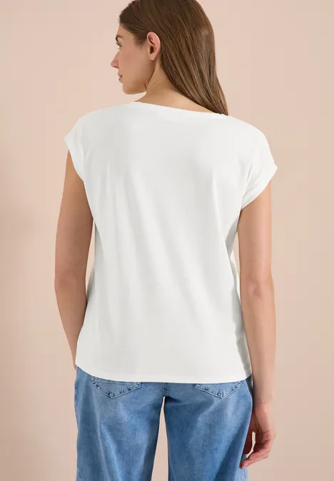 Frau von hinten in weißem T-Shirt und blauen Jeans vor beigem Hintergrund.