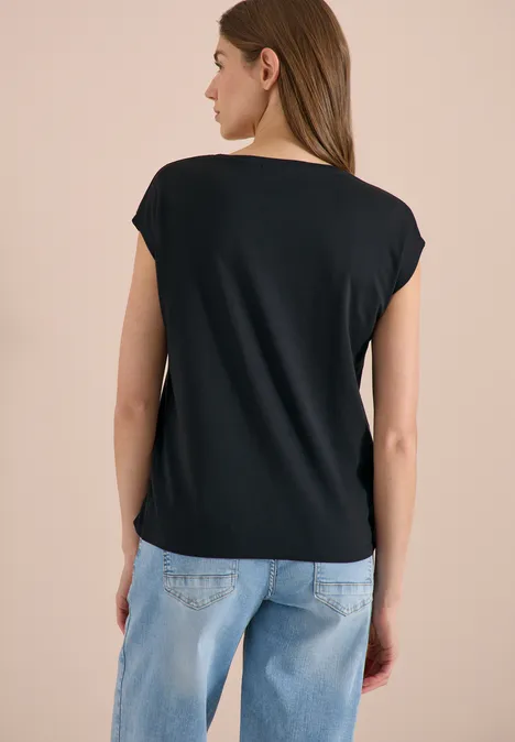 Frau von hinten in schwarzem Shirt und hellblauen Jeans vor neutralem Hintergrund.