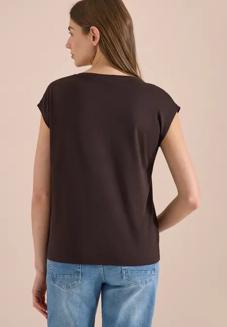 Vrouw van achteren in donker bruin t-shirt en blauwe spijkerbroek voor lichte achtergrond