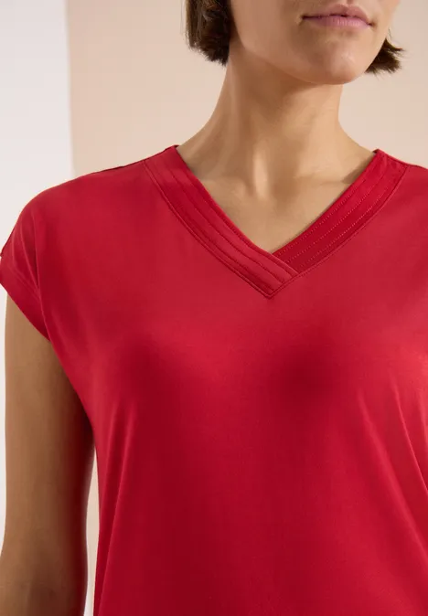 T-shirt à manches courtes et col en V en couleur unie tamarillo red Person en t-shirt rouge col V, gros plan sur le torse et les épaules.