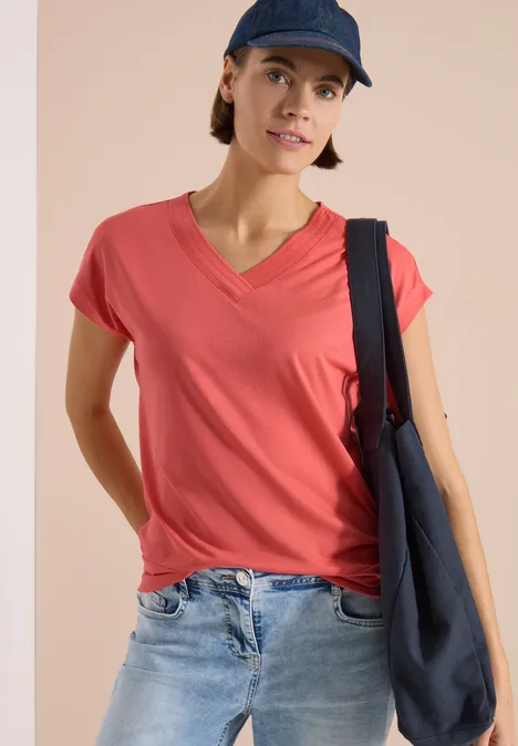 Vrouw in rood V-hals T-shirt, spijkerbroek, donkerblau katoenen tas en pet voor een beige achtergrond