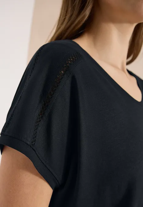 Schwarzes T-Shirt mit V-Ausschnitt und feinem Spitzenbesatz an der Schulter.