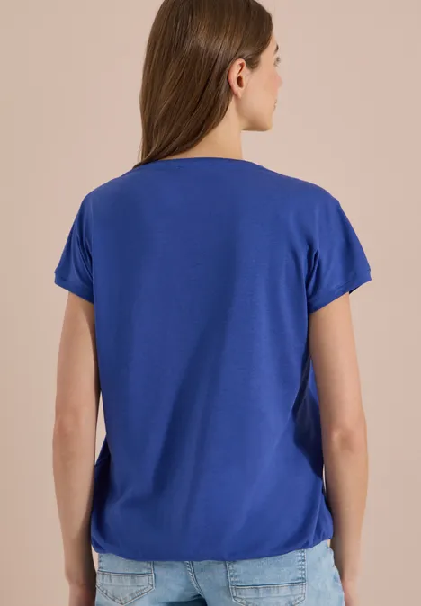 Shirt met V-hals en kanten detail deep river blue Achteraanzicht van een vrouw met halflang haar in een blauw kort mouw T-shirt en een spijkerbroek.