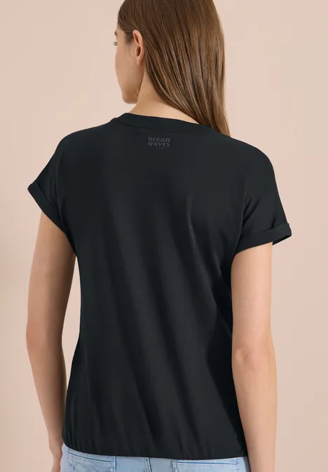 Frau von hinten in schlichtem schwarzen T-Shirt vor beigem Hintergrund