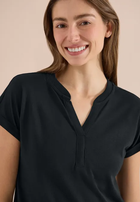 Frau in schwarzem kurzärmligem Shirt mit V-Ausschnitt vor neutralem Hintergrund.