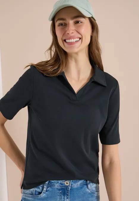 Frau in schwarzem Kurzarmshirt, blauer Jeans und hellblauer Cap vor neutralem beigen Hintergrund.