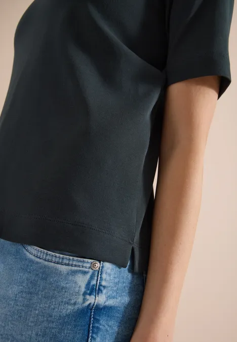 Seitenansicht eines Oberkörpers in dunkelgrünem T-Shirt mit kurzen Ärmeln und blauer Jeans.