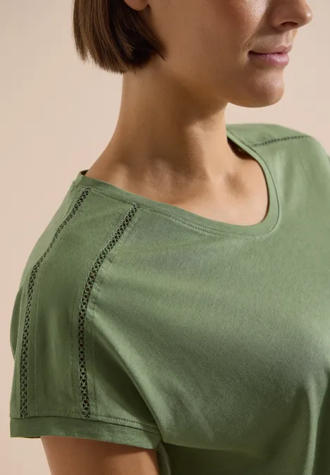 T-Shirt mit V-Neck und Spitzendetail deep matcha green Nahaufnahme einer Frau in olivgrünem T-Shirt mit dekorativer Nahtverzierung an der Schulter.