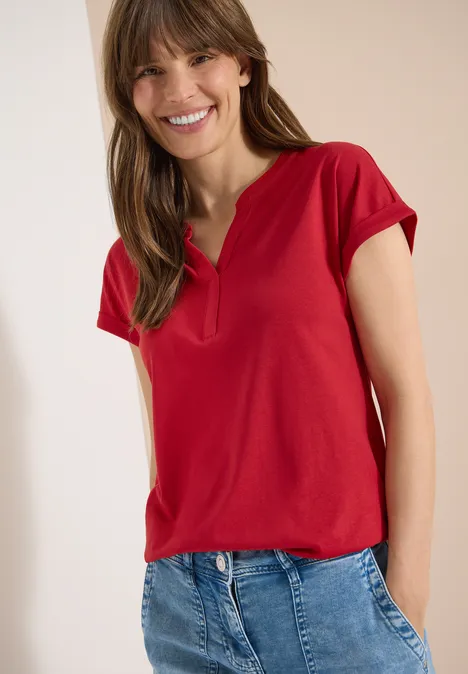 Kurzarm Shirt im Tunika-Look tamarillo red Frau trägt rotes Kurzarmshirt mit V-Ausschnitt und blaue Jeans, Hände in den Hosentaschen.