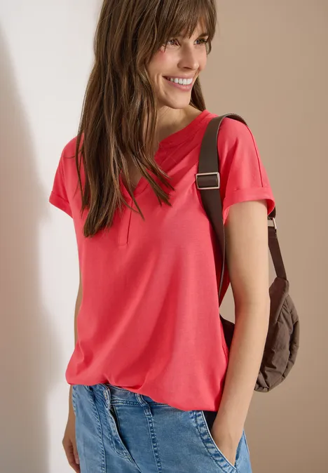 Kurzarm Shirt im Tunika-Look coral Frau in rotem T-Shirt und Jeans mit Rucksack an neutralem Hintergrund.