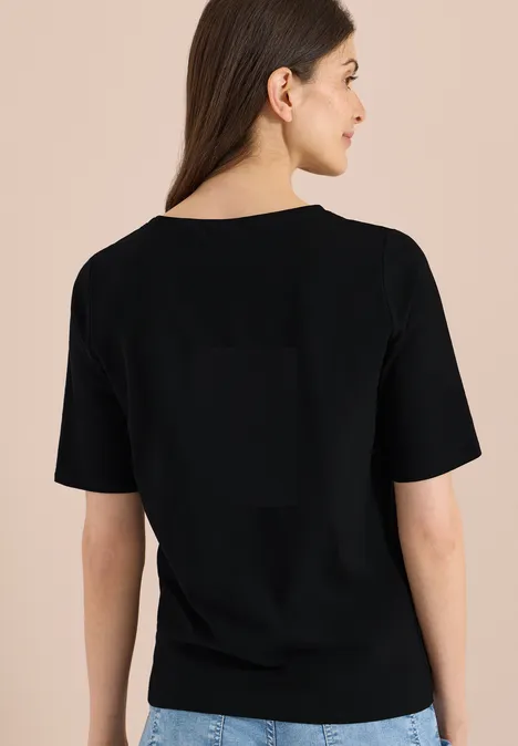 Basic Shirt met boothals Black Vrouw van achteren in een basic zwart t-shirt tegen een neutrale achtergrond.