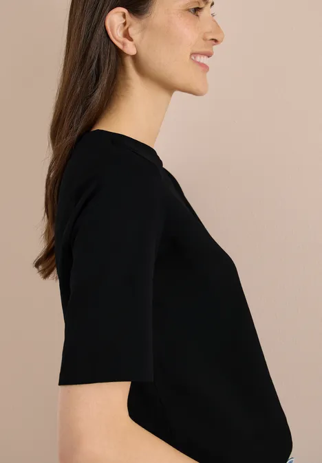Basic Shirt met boothals Black Zijaanzicht van een vrouw in een zwart T-shirt met korte mouwen tegen een neutrale achtergrond, gezicht onscherp.