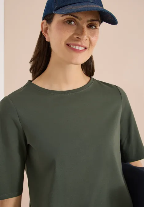 Basic Shirt met boothals khaki Persoon met olijfgroen t-shirt met halve mouwen en pet voor lichte achtergrond.