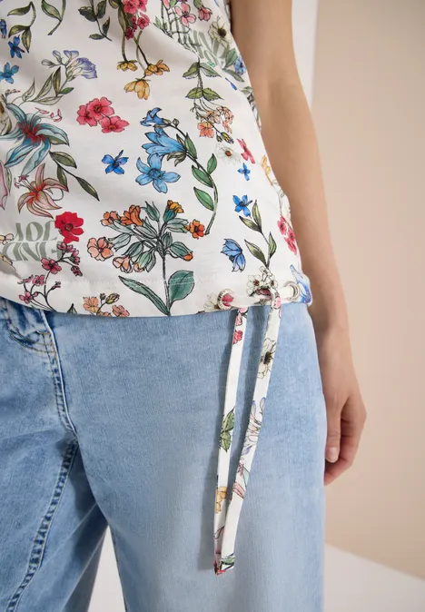 Shirt met bloemenprint light alabaster white Close-up van een vrouw in een gebloemde top met zijstrik en lichtblauwe jeans.