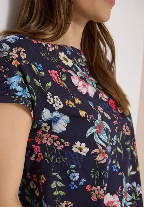 Shirt met bloemenprint universal blue Zijaanzicht van een vrouw in een marineblauw shirt met kleurrijk bloemenpatroon.