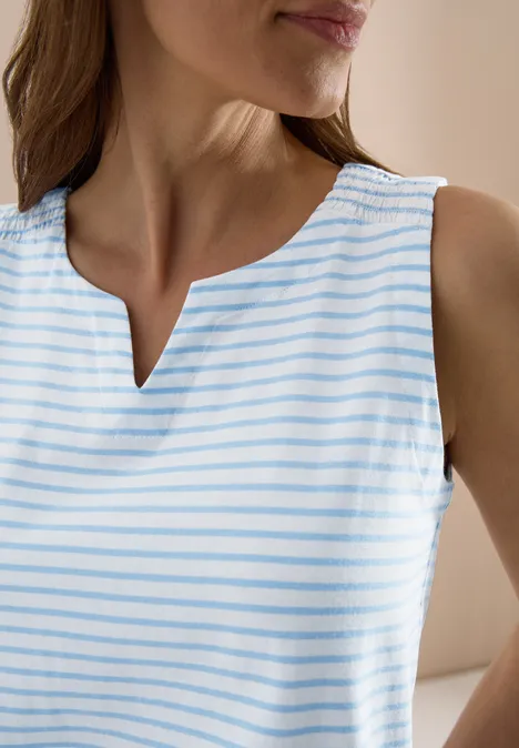 Nahe Aufnahme einer Frau in ärmellosem Top mit weißen und hellblauen Streifen und V-Ausschnitt.