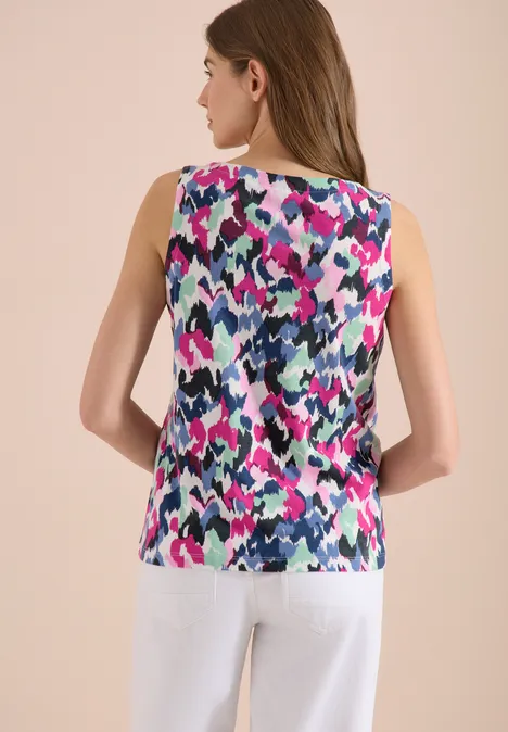 Vrouw van achteren in een mouwloos topje met kleurrijk abstract patroon en een witte broek.