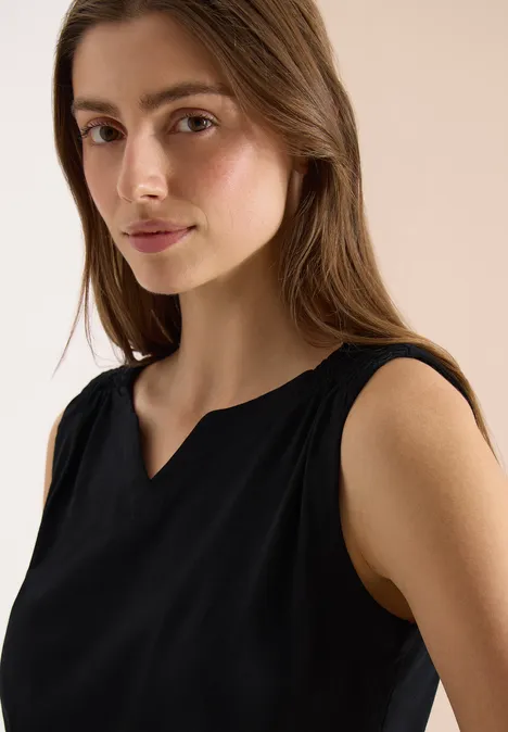 Eine Person trägt ein ärmelloses schwarzes Oberteil vor hellem Hintergrund.