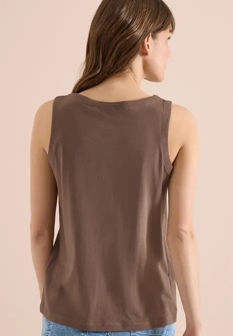 Frau steht mit dem Rücken zur Kamera und trägt ein braunes ärmelloses Oberteil.