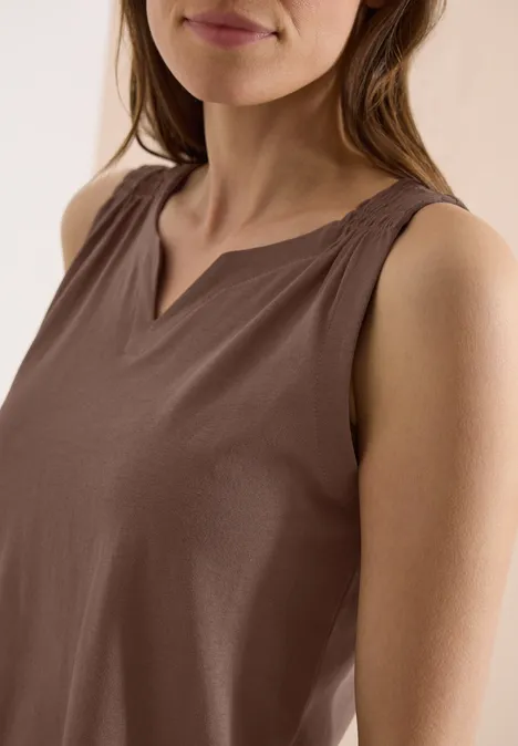 Frau in ärmellosem, braunen Top mit V-förmigem Ausschnitt.