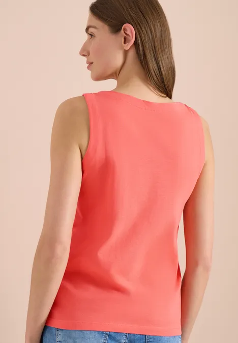 Een vrouw gezien van achteren draagt een koraalkleurige mouwloze top.