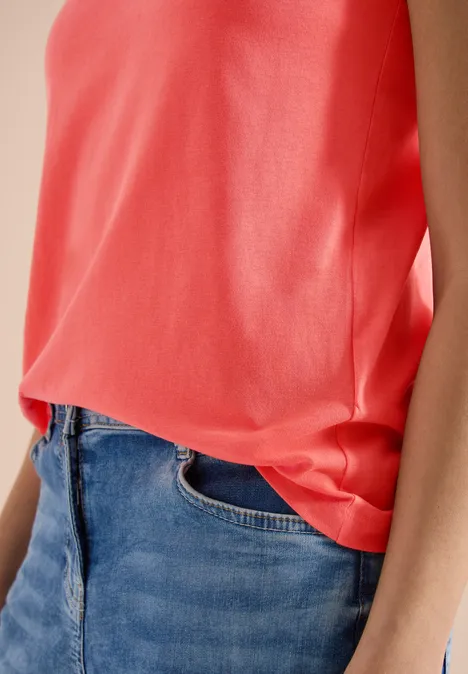 Iemand draagt een mouwloos koraalkleurig topje, ingestopt in een klassieke blauwe spijkerbroek.