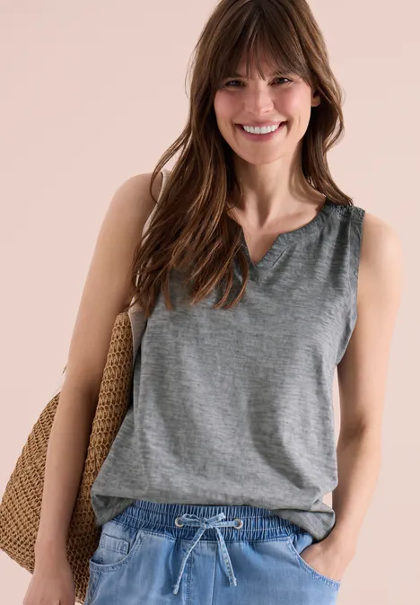 Frau in grauem ärmellosen Top und Jeans, lässig mit Strohtasche.