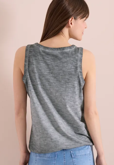 Eine Frau steht von hinten, trägt ein graues ärmelloses Top und blaue Jeans.