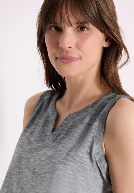 Frau trägt graues, ärmelloses Oberteil mit dezentem V-Ausschnitt und feiner Textur.