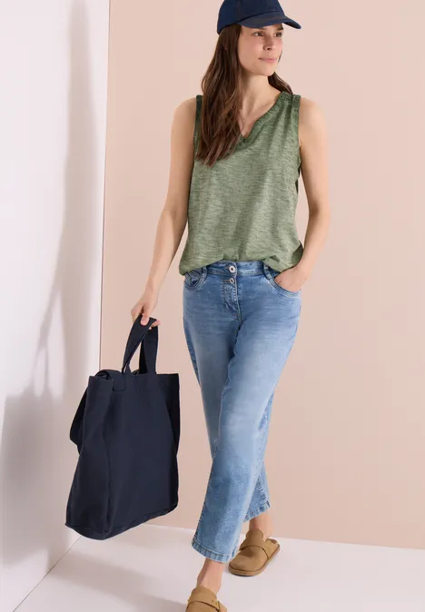 Frau in grünem Tanktop, Jeans und Cap trägt große schwarze Tasche und beige Schuhe.