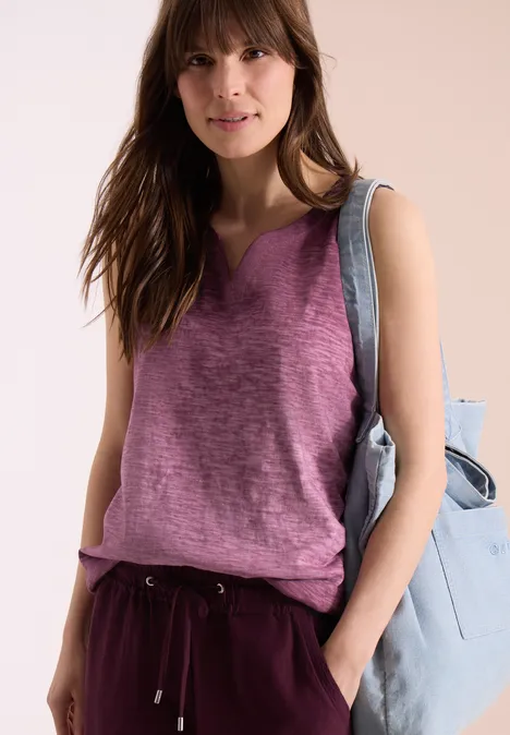 Frau in ärmellosem lila Top und schwarzer Hose mit hellblauer Umhängetasche