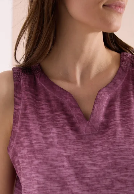 Eine Frau trägt ein ärmelloses meliertes Top in Violett; man sieht Brust- und Halsbereich.