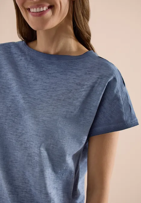 Ausschnitt einer lächelnden Person in einem kurzärmeligen, blauen T-Shirt.