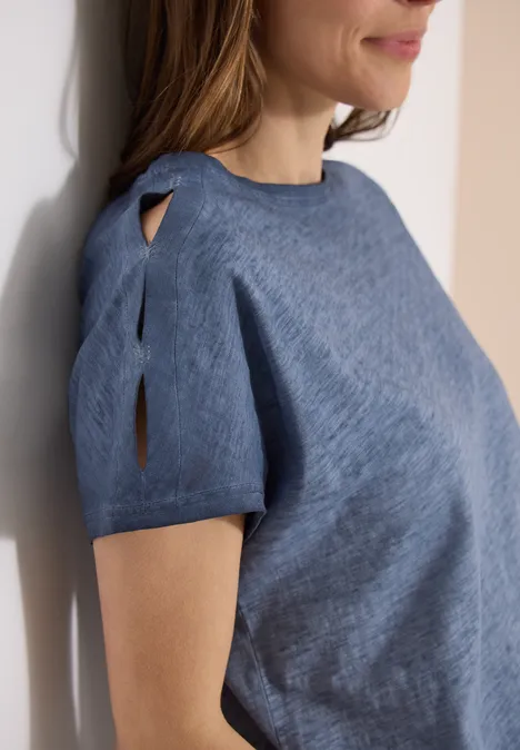 Nahaufnahme einer Frau in einem blauen, kurzärmligen Pullover mit Schlitz am Ärmel und rundem Ausschnitt.