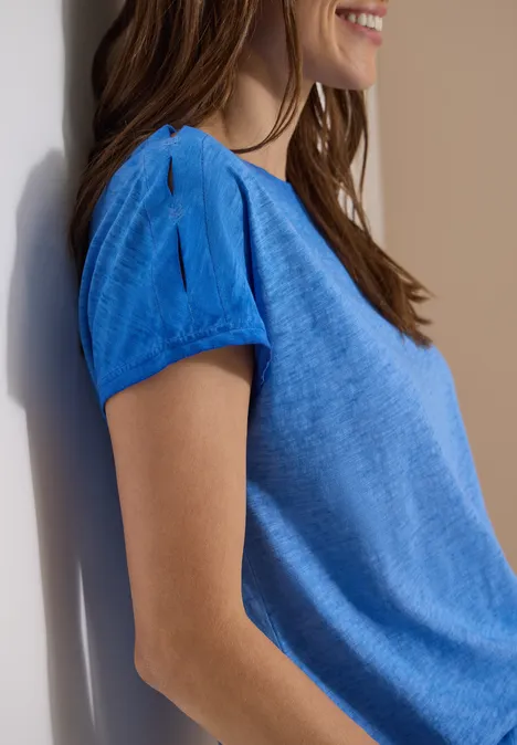 Shirt van geverfde jersey surf blue Close-up van een glimlachende vrouw in een lichtblauw kort T-shirt, zijkant, voor een witte achtergrond.