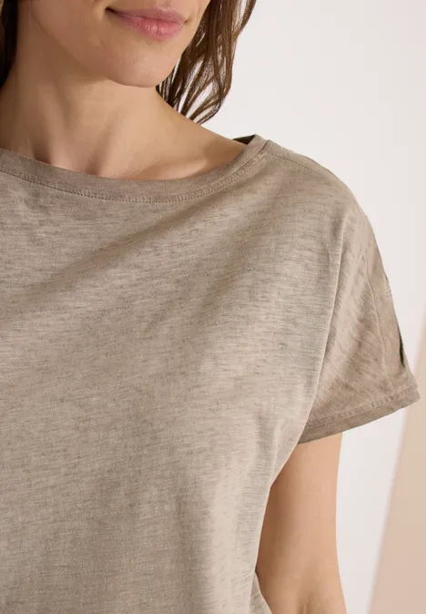 Nahaufnahme einer Frau in beigem T-Shirt mit kurzen Ärmeln und Schulterdetail.