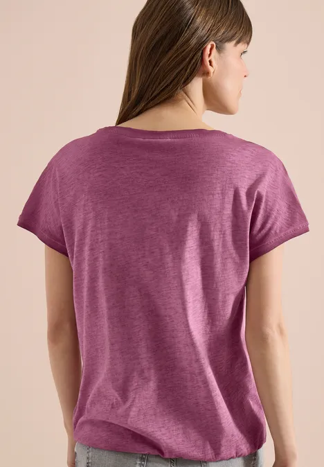 Rückenansicht einer jungen Frau mit langem braunem Haar, die ein kurzärmeliges lila T-Shirt trägt.