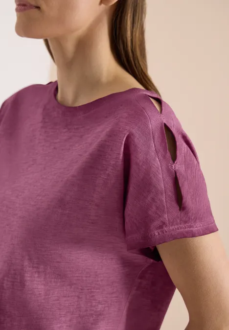 Frau trägt eine kurzärmelige, purpurfarbene Bluse mit Schulterauschnitten aus Leinen.