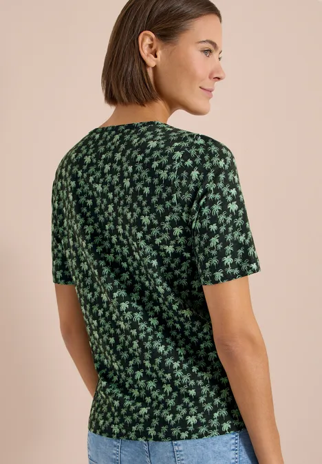 Frau trägt grünes, kurzärmeliges Shirt mit kleinem floralen Muster, Rückenansicht.