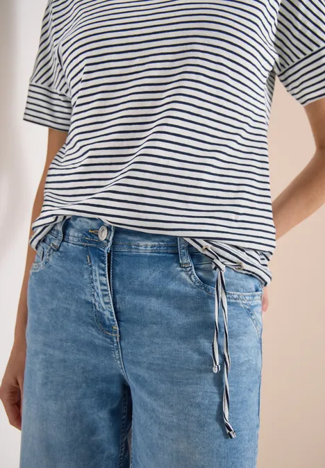 Person mit weiß-schwarz gestreiftem T-Shirt, locker in eine blaue Jeans mit Kordelzugbund gesteckt.