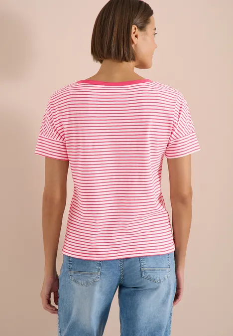 Rückenansicht einer Person in rosa-weiß gestreiftem T-Shirt und hellblauen Jeans vor beigem Hintergrund.